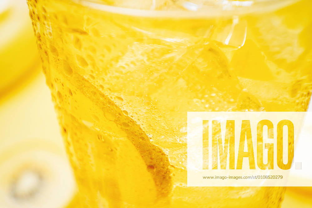 From above crop detail of glass of fresh beverage with lemons and kiwi placed in yellow background in studio