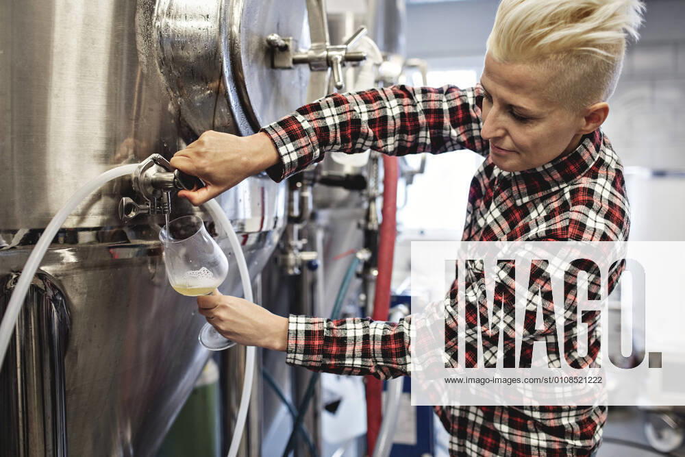 Confident female manager pouring beer from storage tank at factory , model released, property released