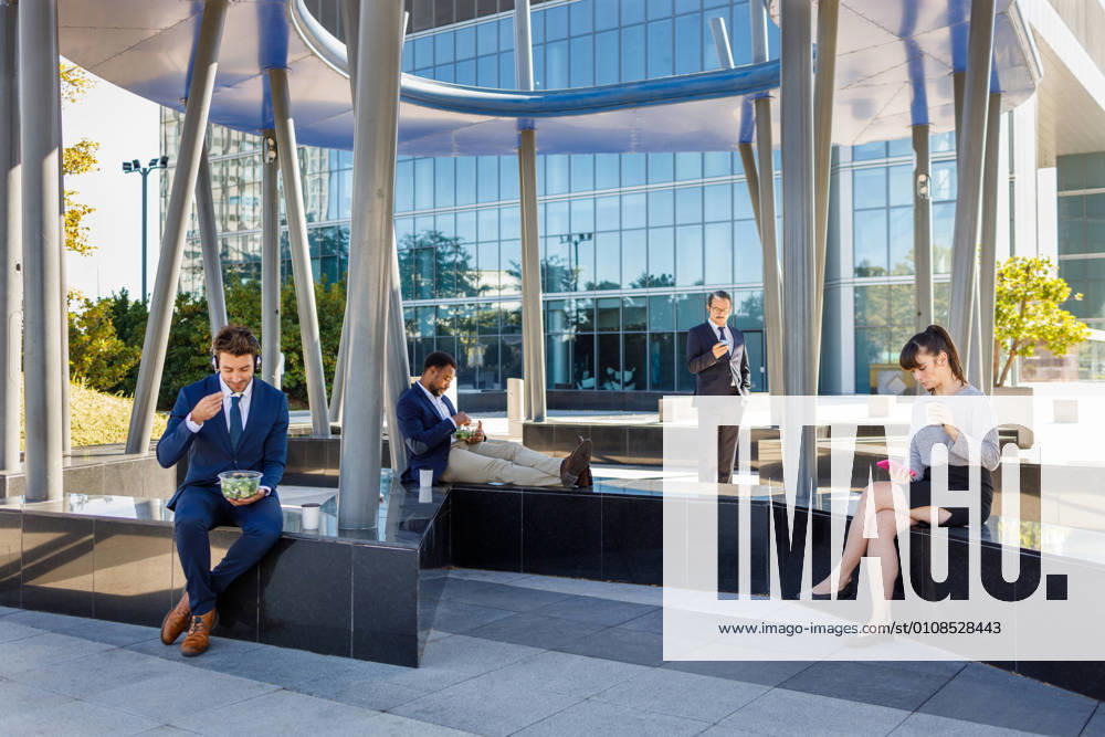 Group of young multiracial coworkers in classy outfits sitting on bench near modern business center and having lunch, Model released