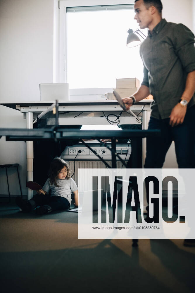 Full length of businessman playing table tennis while boy using laptop at creative office , model released, property released