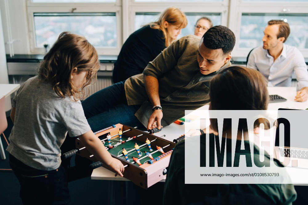 High angle view of boy playing foosball with businessman on desk amidst colleagues at creative office , model released, property released