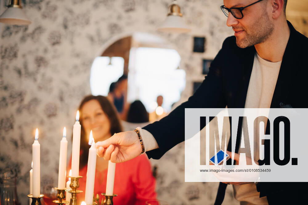 IMAGO Creative: Guten Rutsch IMAGO Creative: Landleben - Essen Smiling man igniting candles at dinner party with friend in background , model released, property released