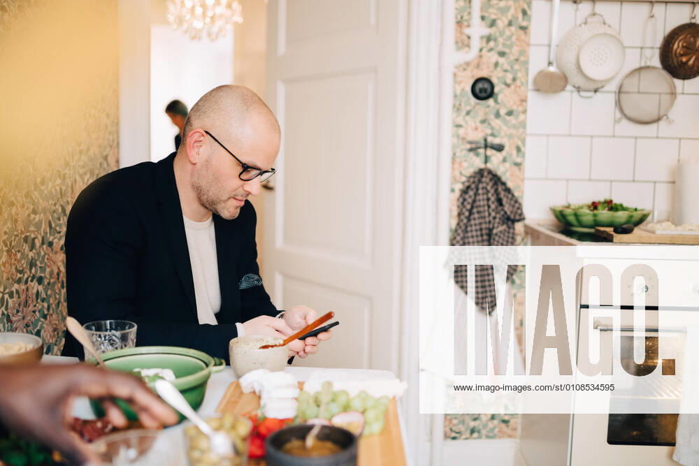 IMAGO Creative: Landleben - Essen Mature man using mobile phone while sitting at dining table during party , model released, property released