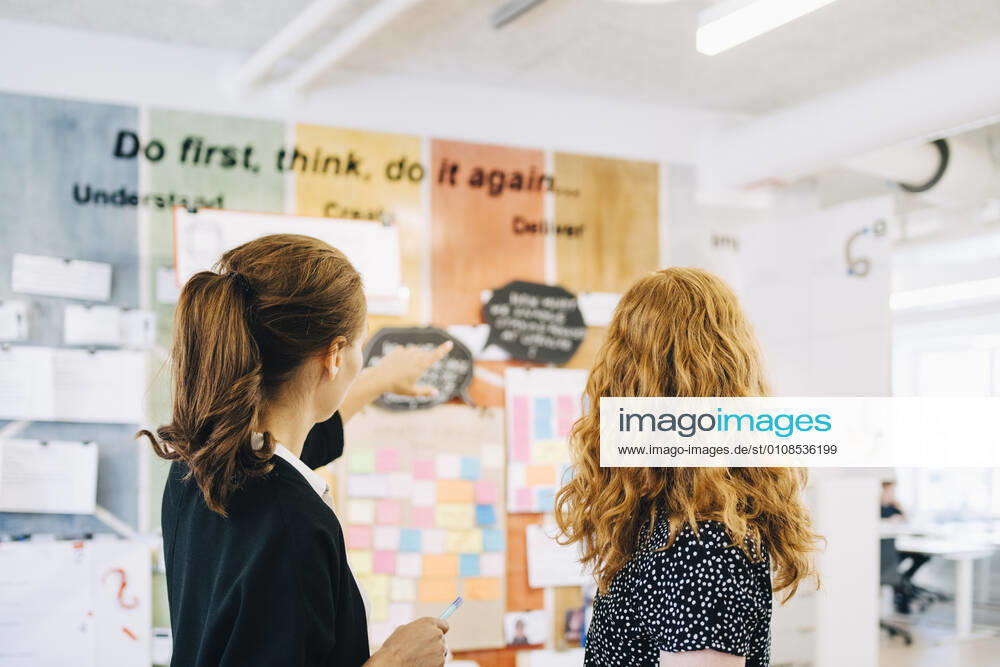 Confident female colleagues discussing over strategy on wall at creative office , model released, property released