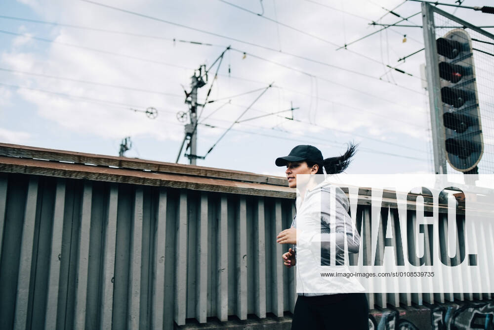Young sportswoman jogging by fence on footbridge in city , model released