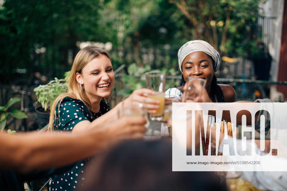 Multi-ethnic friends toasting drinks while sitting at balcony , model released, property released