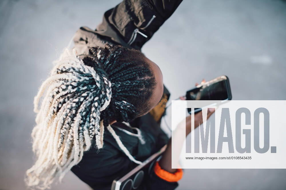IMAGO Creative: Sport Start-Up High angle view of teenage girl with dreadlocks dancing while holding smart phone at skateboard park , model released