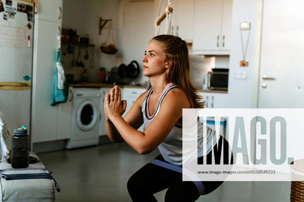 Side view concentrated young sportswoman in activewear squatting with resistance band on heaps while training at home