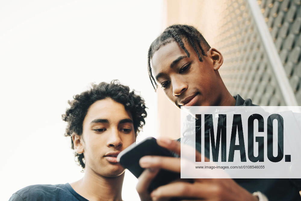Low angle view of teenage boy showing mobile phone to friend in city , model released