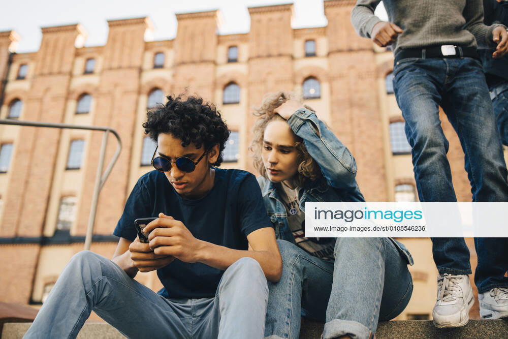 Teenage boy using mobile phone while sitting by friend in city , model released