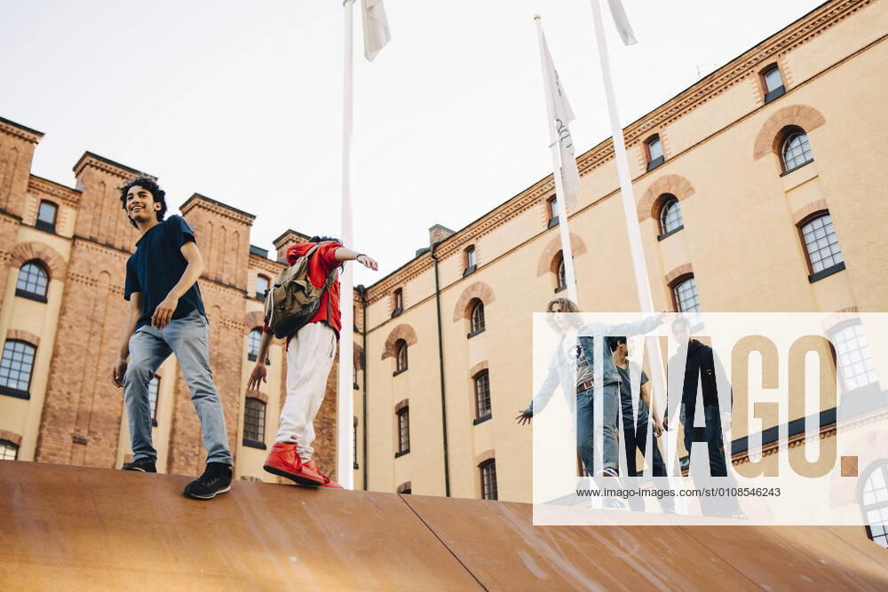 Low angle view of carefree playful friends walking on wall in city , model released