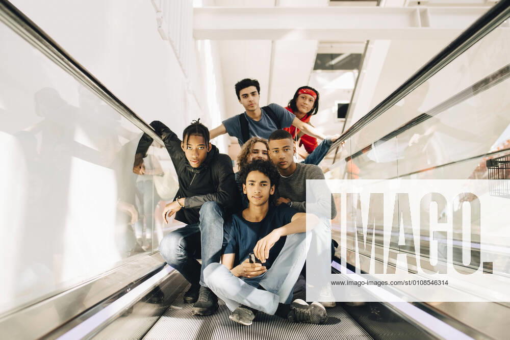 Portrait of confident male friends on moving walkway in shopping mall , model released