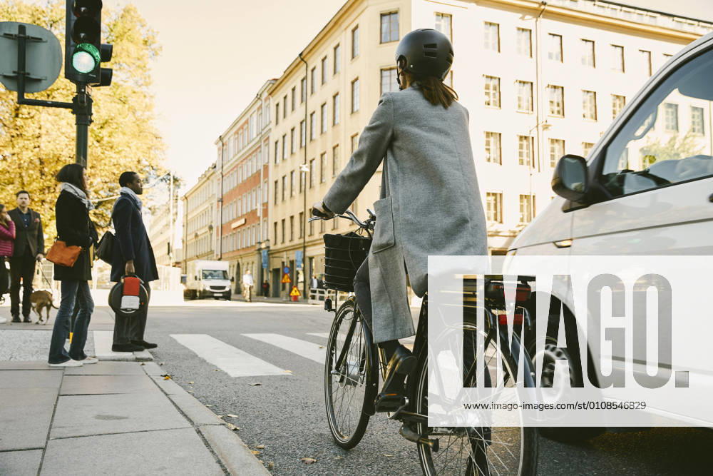 IMAGO Creative: Klimawandel - Zukunft und Innovation Rear view of woman riding electric bicycle by car on street in city , model released