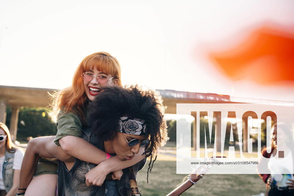 Young man piggybacking happy friend while enjoying in music festival , model released