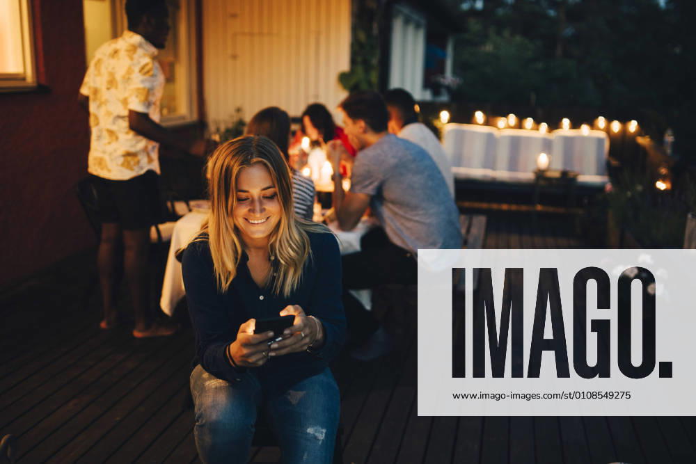 Smiling young woman using smart phone while friends in background at dinner party , model released, property released
