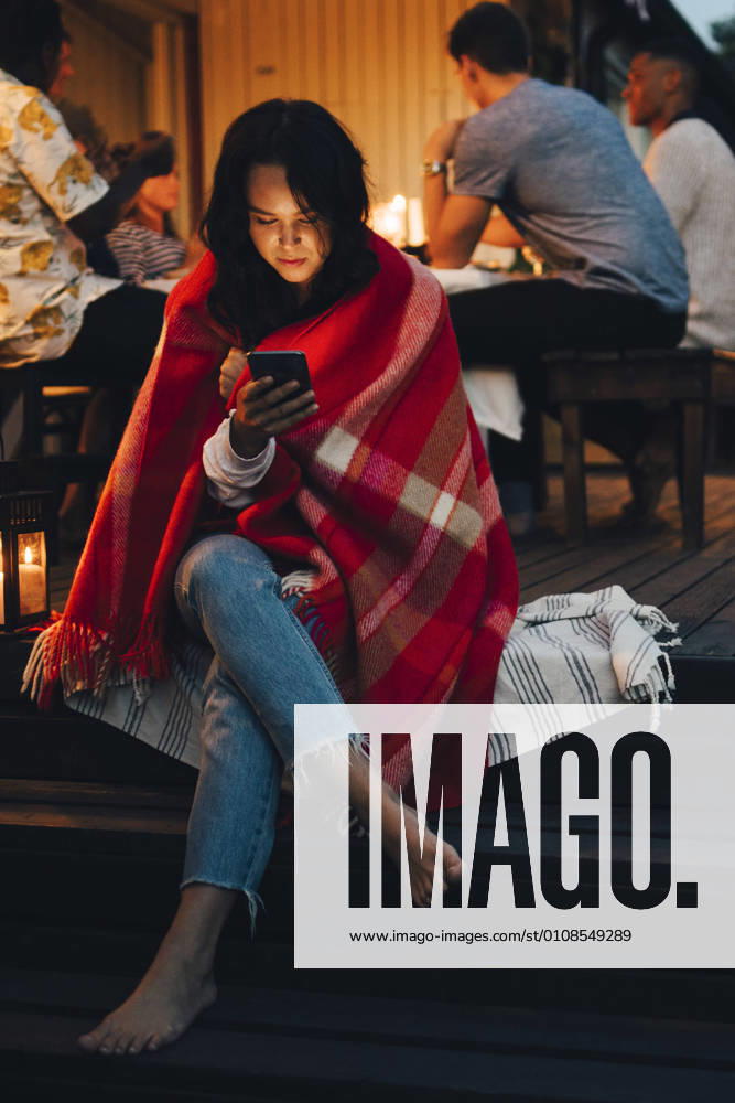 Young woman using smart phone while friends in background during dinner party , model released, property released