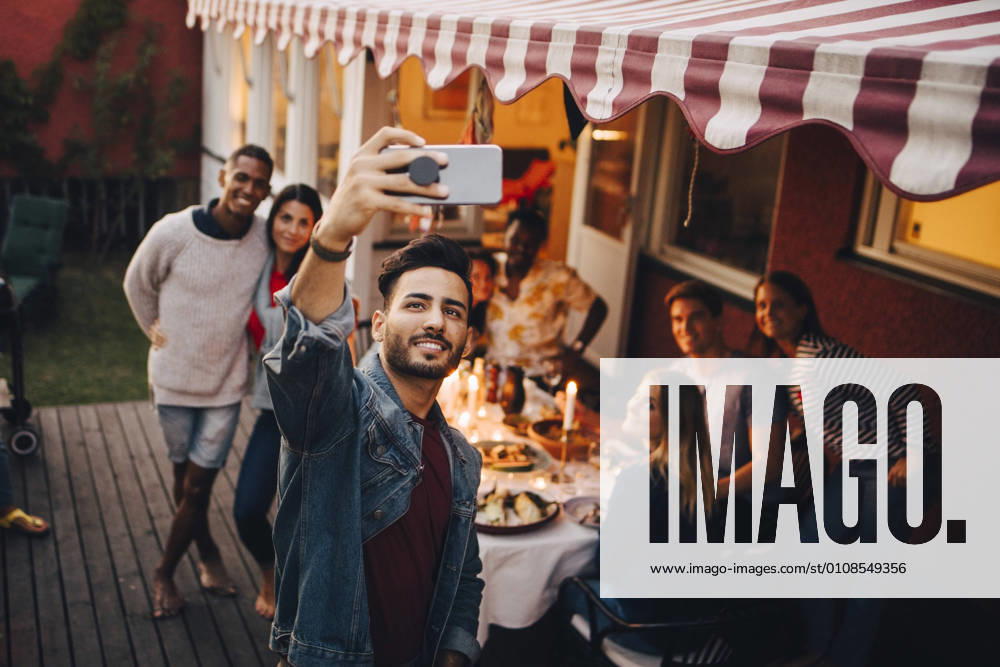 Smiling young man taking selfie with friends during dinner party , model released, property released