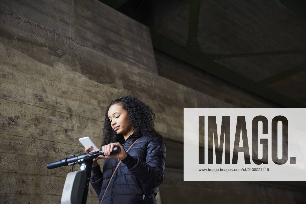 IMAGO Creative: Business, Innovative Technologie-Lösungen Low angle view of teenage girl with electric push scooter using mobile phone by wall below bridge , model released