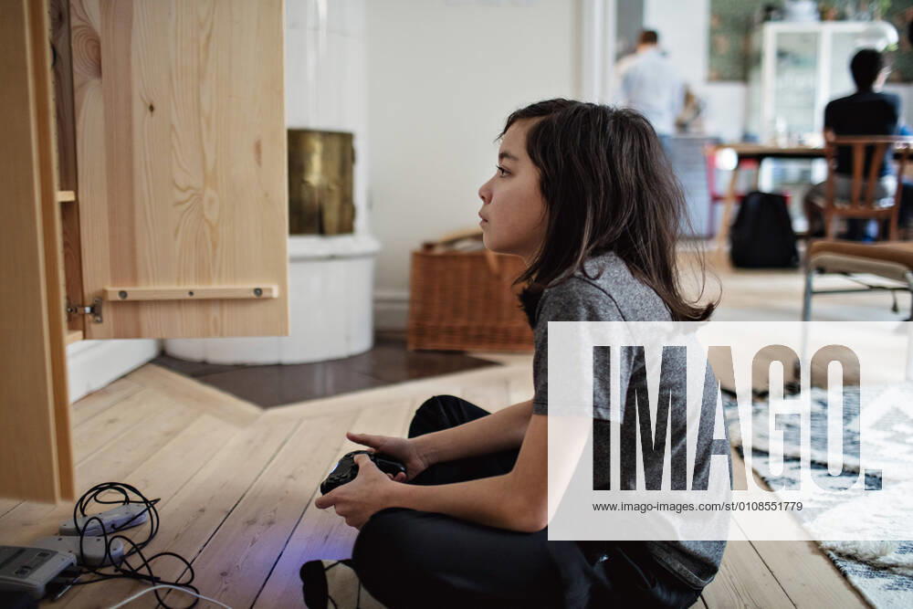 Side view of boy looking away while playing video game on hardwood floor at home , model released, property released