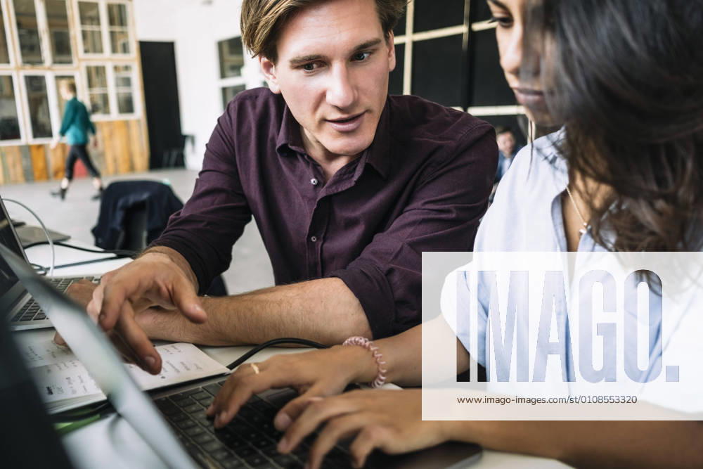 Confident male IT professional discussing with female hacker using laptop at desk in creative office , model released, property released