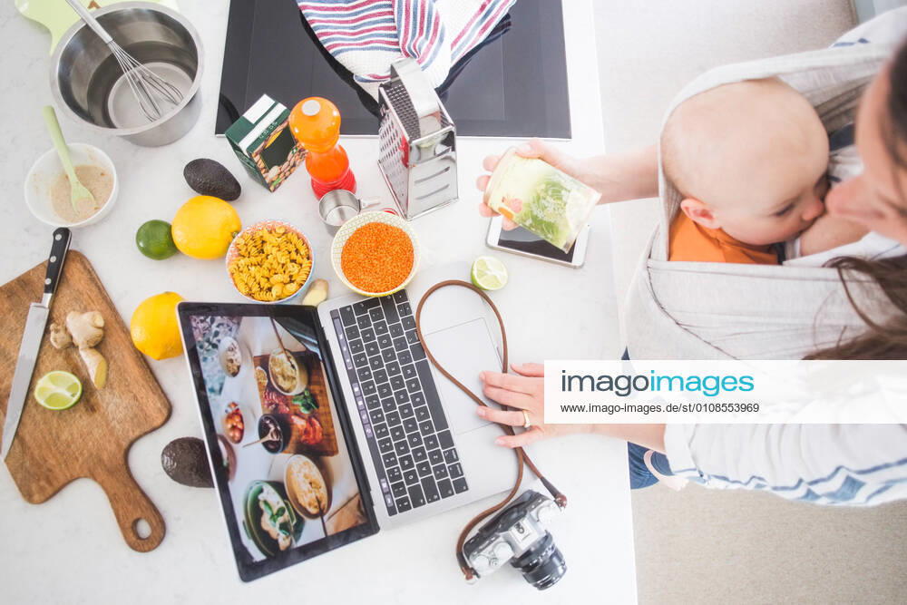 High angle view of female influencer food blogging while breastfeeding baby girl in kitchen , model released, property released