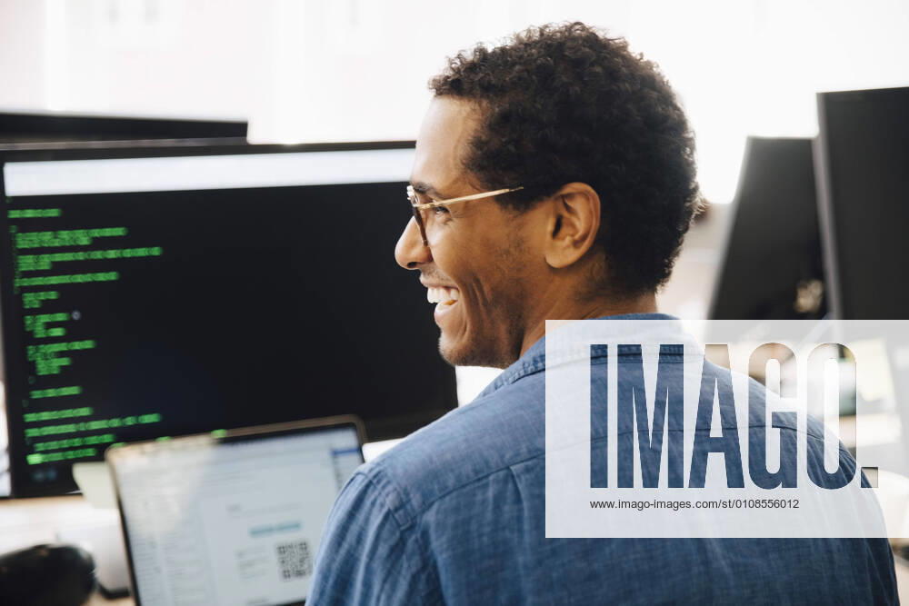 Rear view of cheerful male it professional looking away while sitting in creative office , model released, property released
