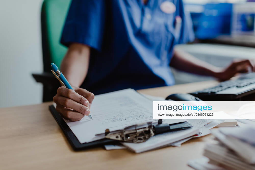 Midsection of nurse writing medical report while sitting at desk in clinic , model released, property released