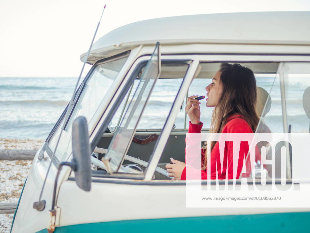 Side view of young woman coloring lips sitting in front seat of car at seaside