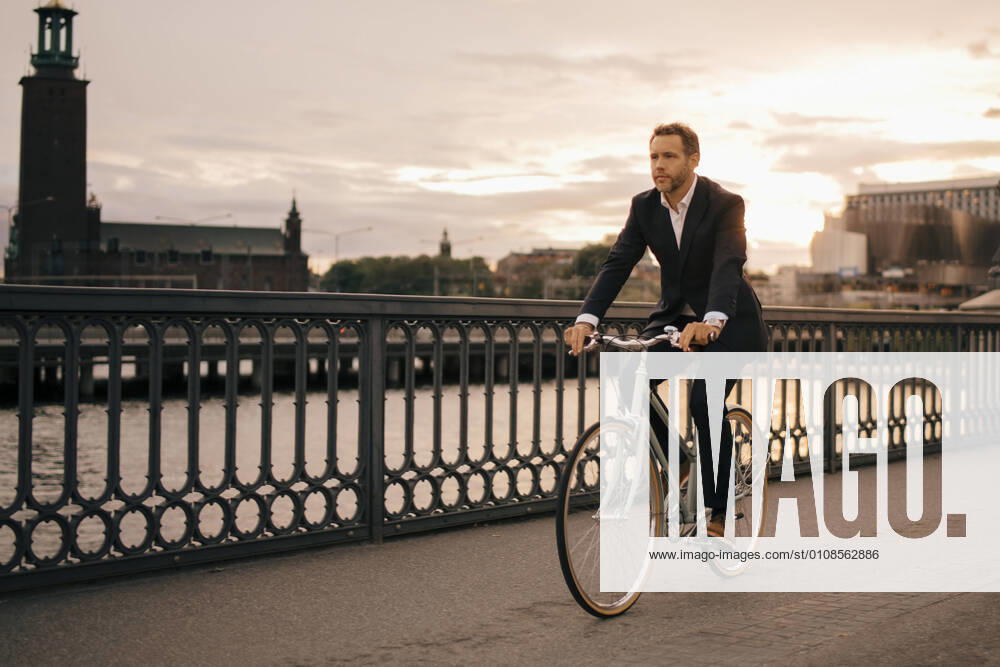 Full length of businessman cycling on bridge in city during sunset , model released