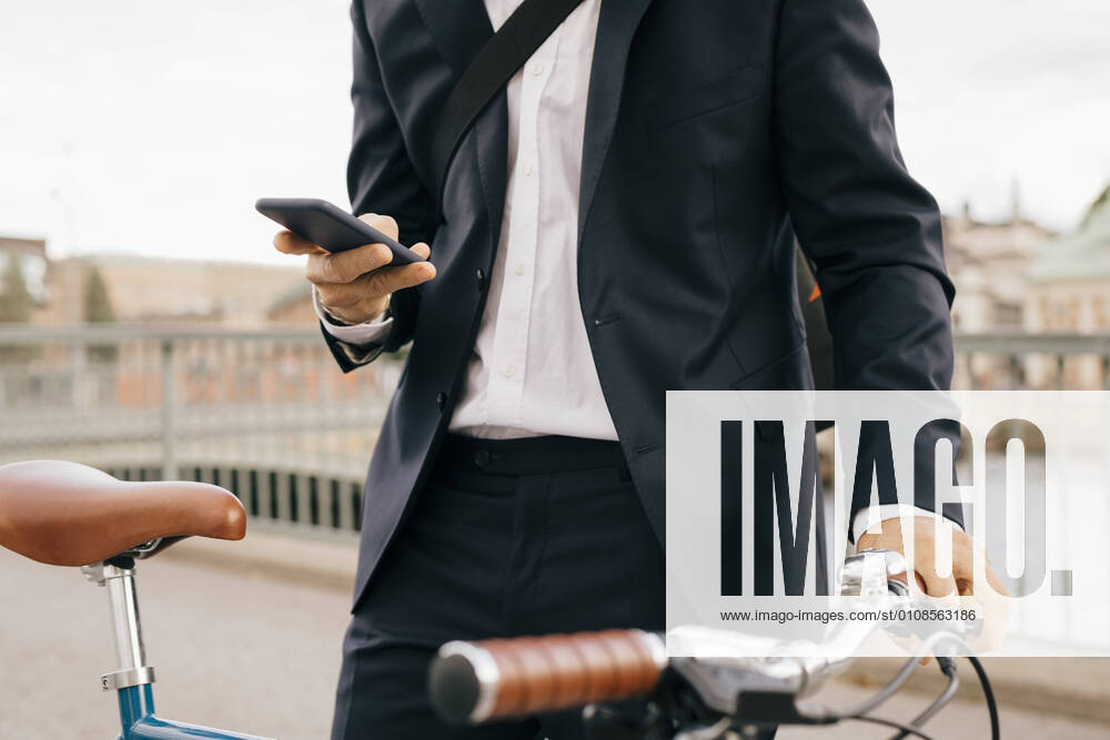 IMAGO Creative: Corporate: Klimaschutz, Digitalisierung und Urbanisierung Midsection of businessman using smart phone while standing with bicycle on bridge in city , model released