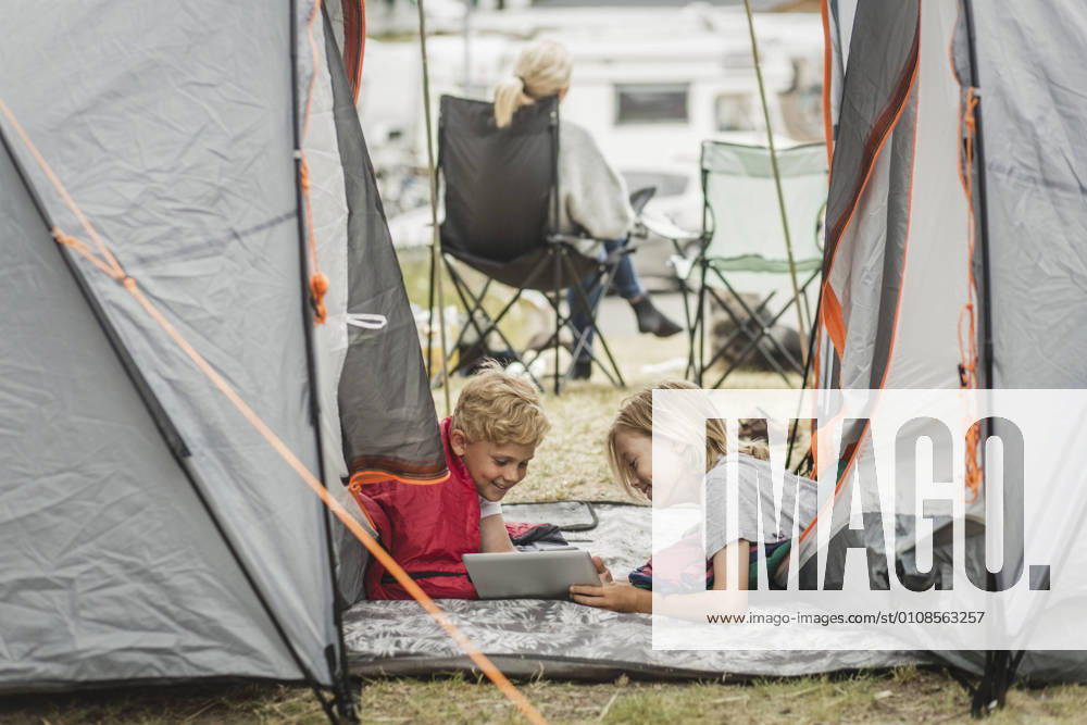 IMAGO Creative, Jahreszeit Sommer, Sommerferien Smiling sister showing digital tablet to brother in tent at campsite , model released, property released