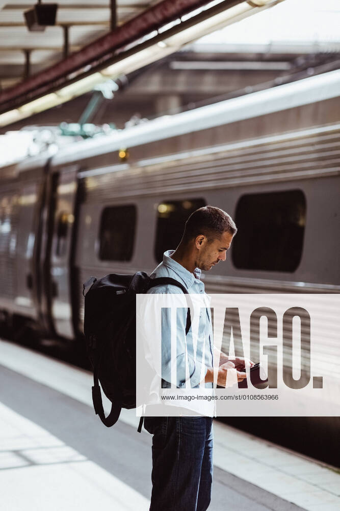 IMAGO Creative: Business, Innovative Technologie-Lösungen Mid adult man with backpack using mobile phone while standing by train on platform , model released, property released