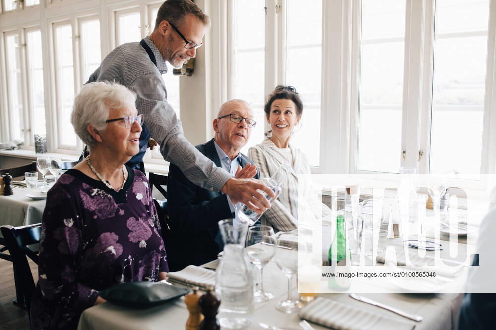 Owner serving water to senior people sitting at restaurant , model released, property released