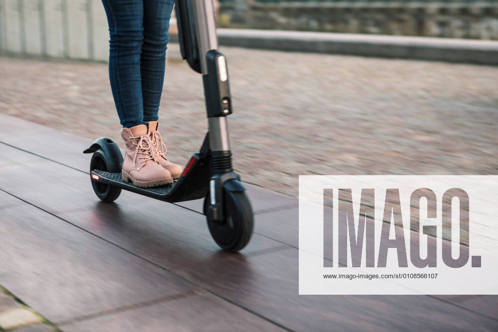 Low section of teenage girl riding on electric push scooter on street , model released