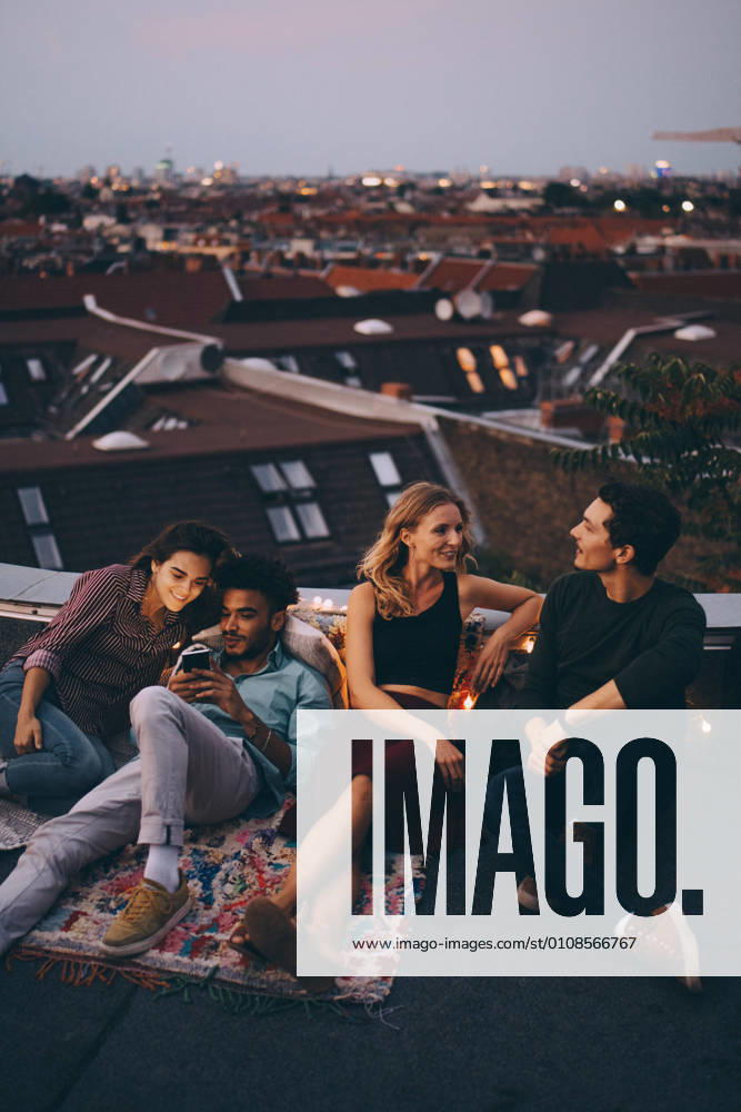 IMAGO Kreativ: Urbane Kultur - Sommer auf den Dächern IMAGO Creative: Menschen in Berlin High angle view of friends relaxing together on terrace in city during rooftop party , model released, property released