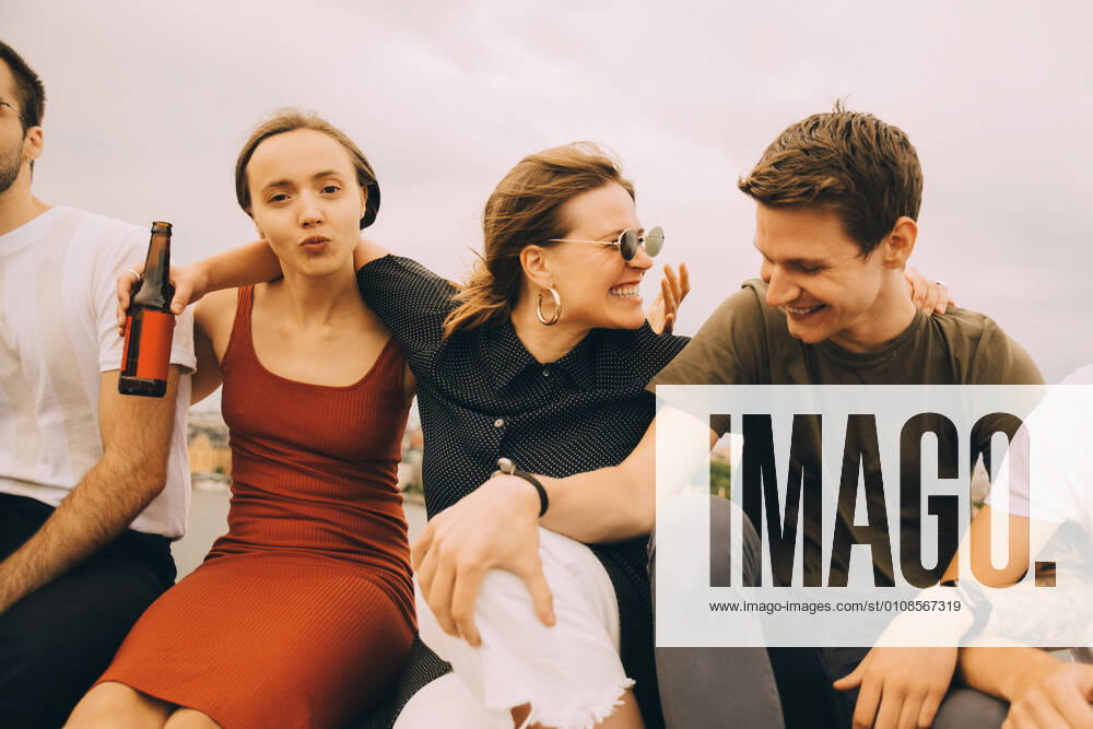 Cheerful friends talking while sitting together against sky , model released