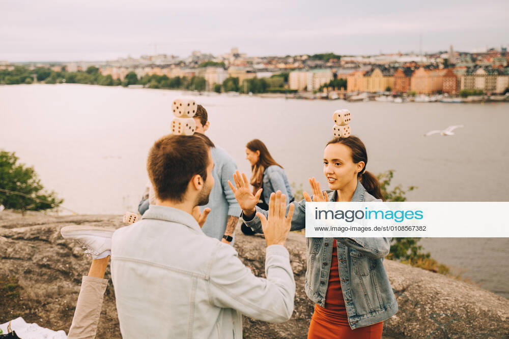 Male and female friends playing balancing games while standing on field by lake , model released