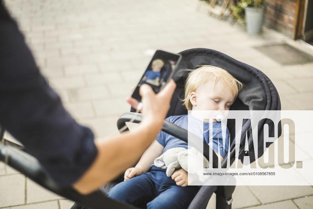 Hand of father photographing sleeping son on baby stroller in city , model released