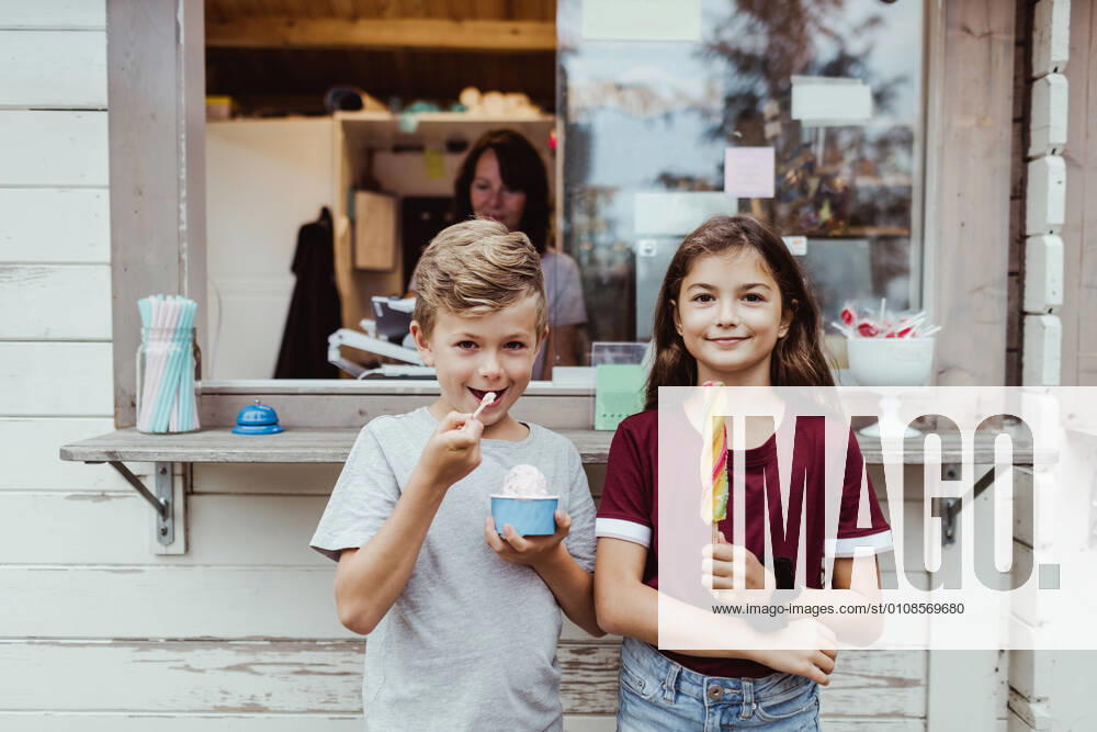 IMAGO Creative: Landleben - Essen Portrait of sibling eating sweet food while standing against concession stand , model released, property released
