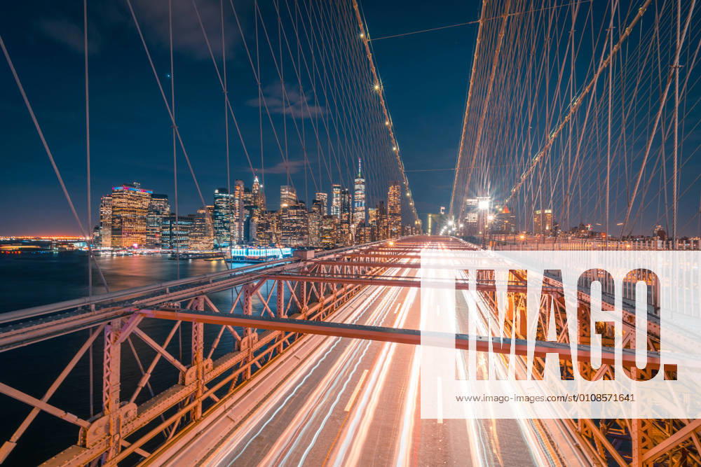 Empty roadway of illuminated Brooklyn bridge at night time with glowing skyscrapers in background in New York City, Model released