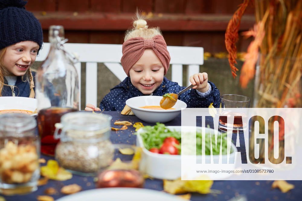 IMAGO Creative: Veganuary, fleischlos leben Smiling girl having vegetarian soup while sitting by female sibling at table , model released, property released