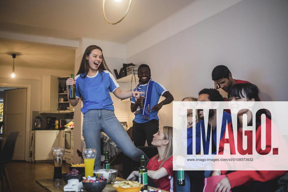 IMAGO Creative: 2022 Aussichten Smiling woman pointing at female while watching sport with friends at home , model released, property released