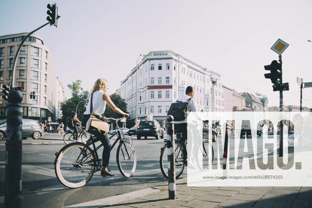 Full length of male and female entrepreneurs riding bicycle on road in city , model released