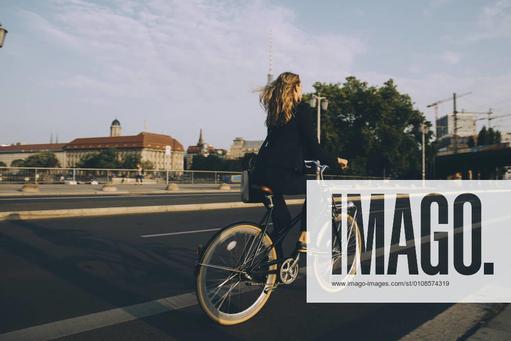 Rare view of female executive riding bicycle on road in city against sky , model released