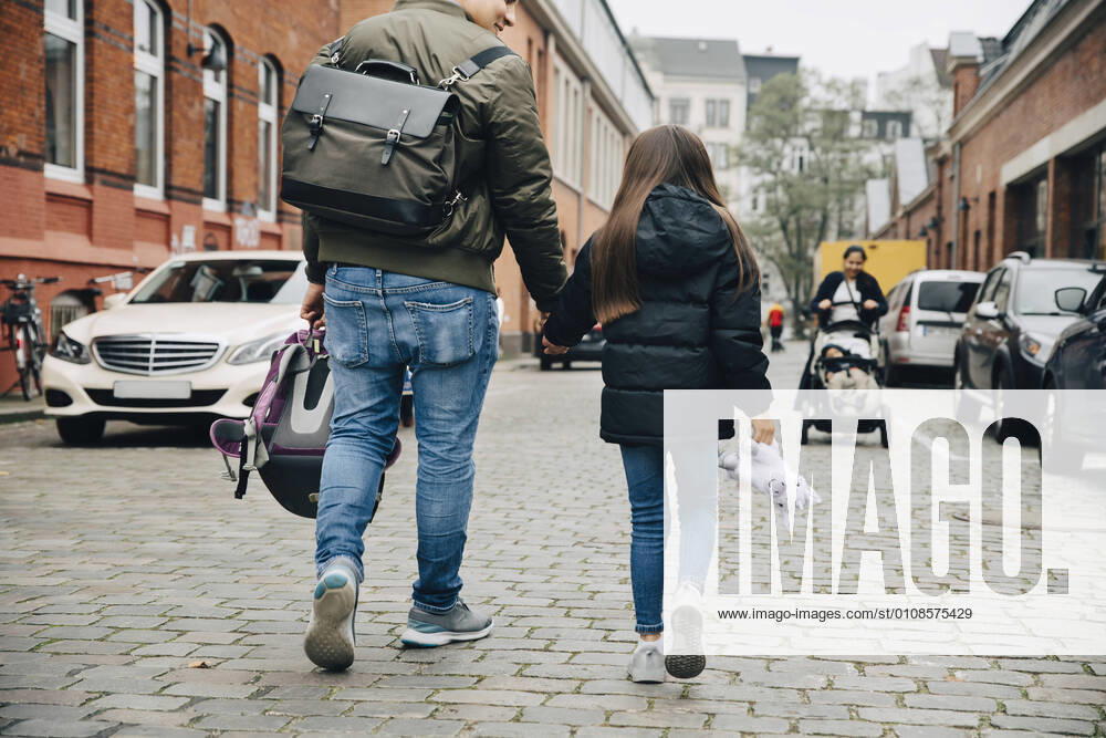 Rear view of father and daughter holding hands walking on footpath in city , model released