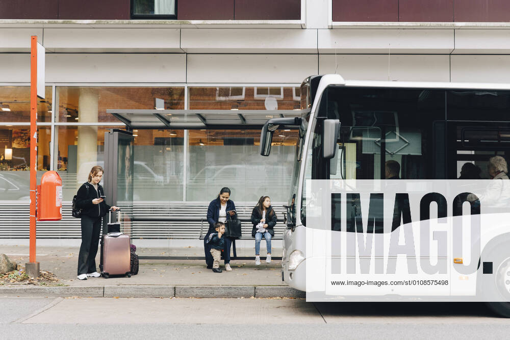 Full length of woman with luggage and family waiting for bus at bus stop in city , model released