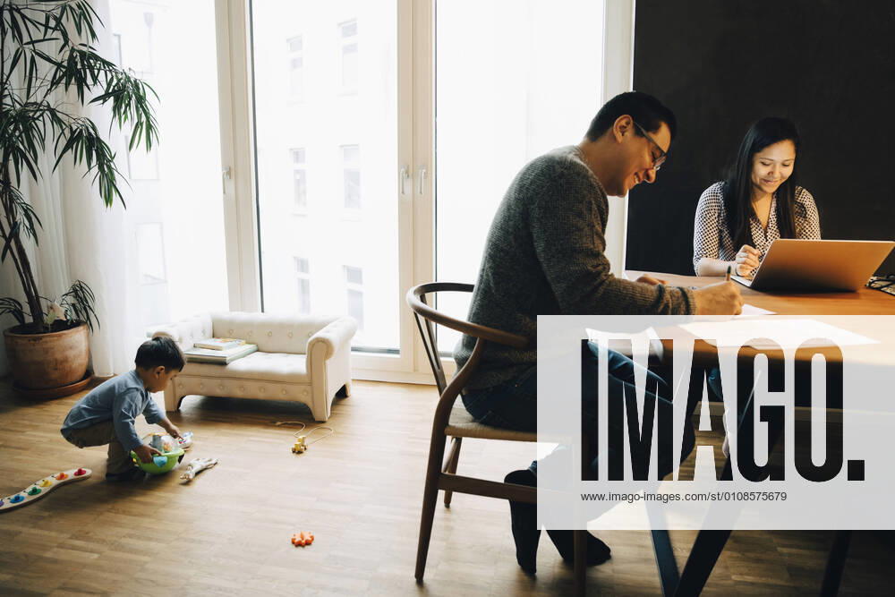 IMAGO Creative: 2022 Aussichten Mother and father working at dining table while son playing with toys in living room , model released, property released
