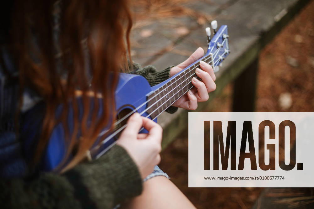 IMAGO Creative: Digitale Welt, Verzicht auf Technologie From above unrecognizable brunette in casual clothes playing small blue guitar while sitting alone on wooden bench in autumn city park