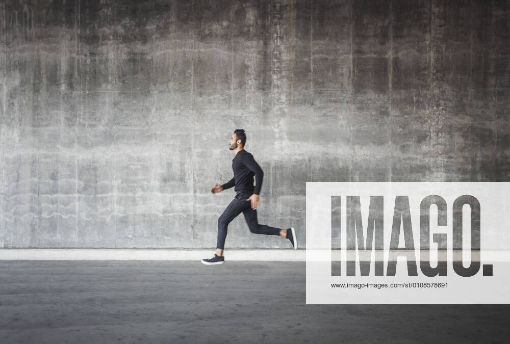 Side view of young man running by gray wall , model released