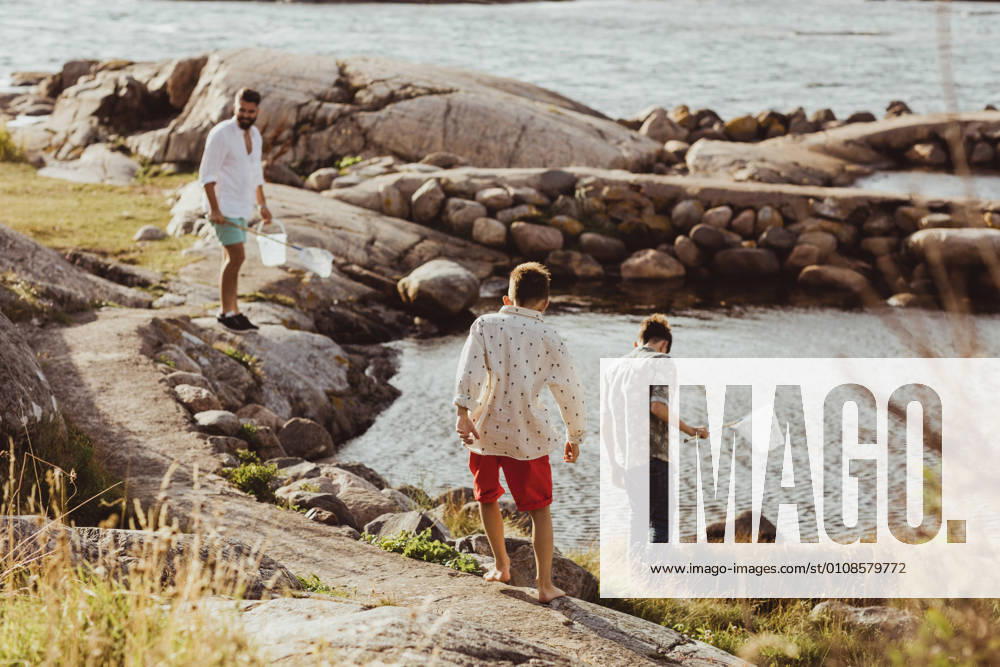 IMAGO Creative, Jahreszeit Sommer, Sommerferien Rear view of boy with sibling while father standing over rock during weekend Sweden, Gothenburg, model released